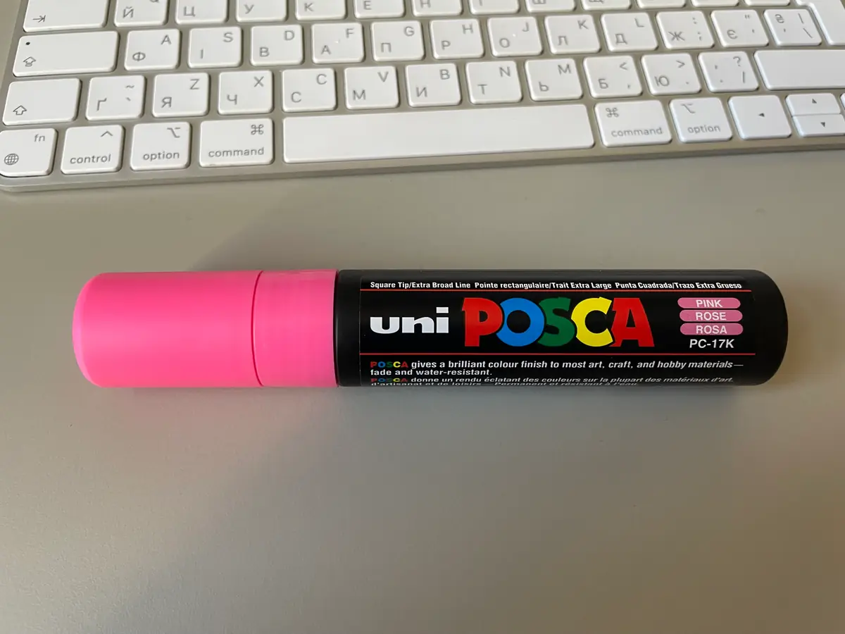 A black POSCA PC-17K paint marker with a pink cap lying on a laptop.